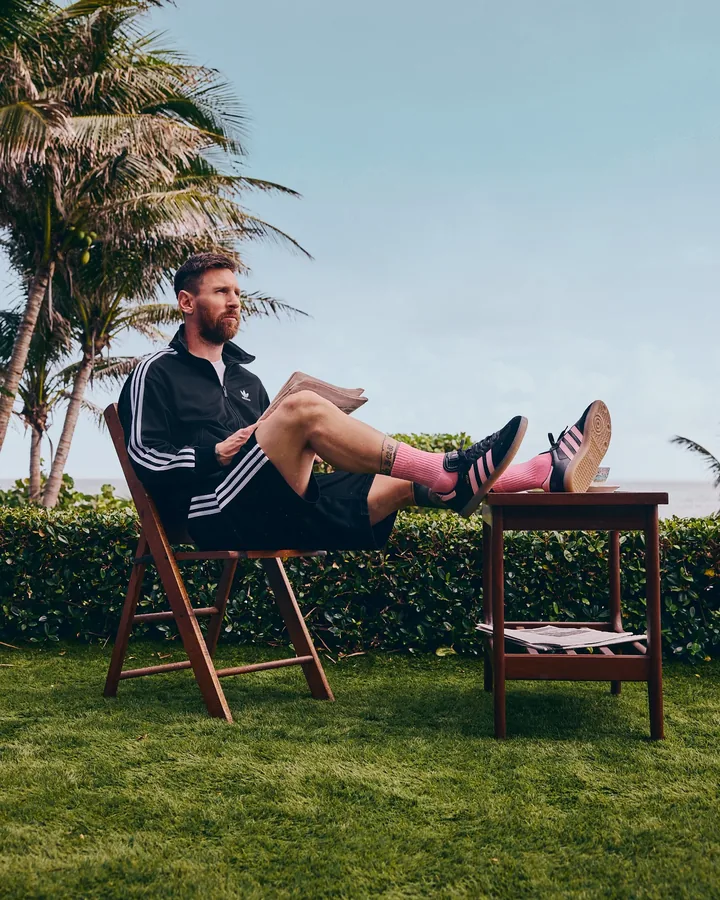Lionel Messi seated on a lawn in adidas with his feet on a table, wearing pink socks and Sambas