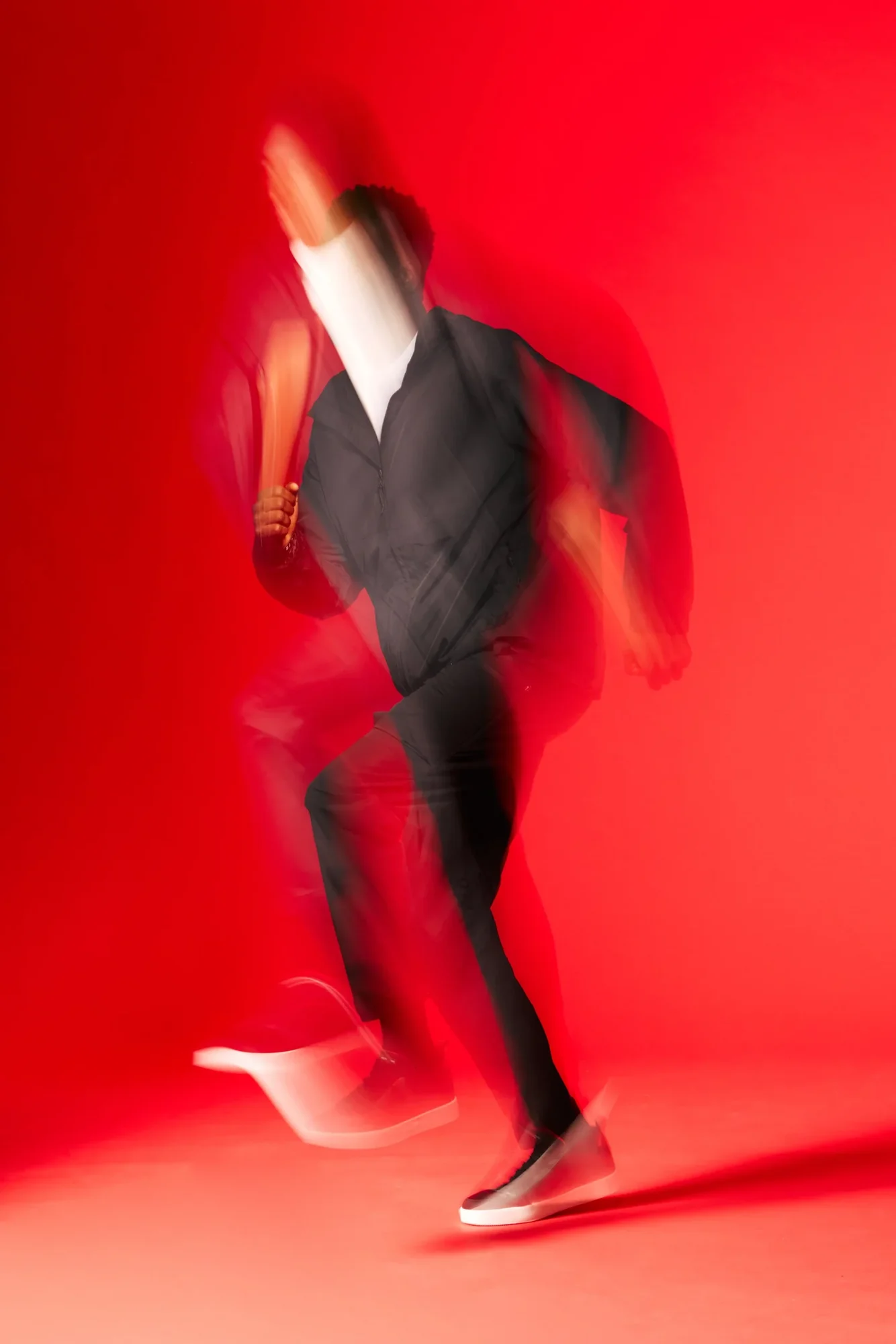 Long-exposure motion-blur figure in dark clothing against a vivid red background for Atoms x MKBHD