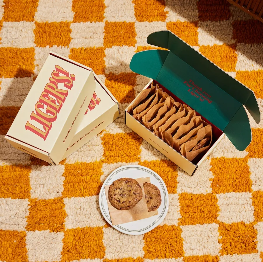 Two Liger's cookie boxes on an orange and cream checkered rug beside cookies on a plate