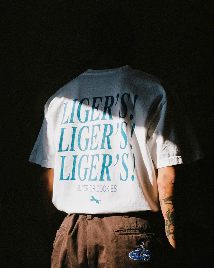 Back of a white Liger's t-shirt in dramatic shadow with repeated blue type